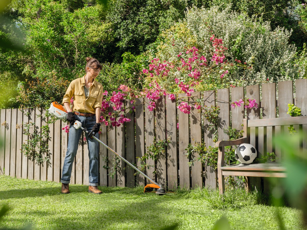 Frau verwendet FSA 80 R US im Garten und schneidet die Rasenkante vor einem Zaun 