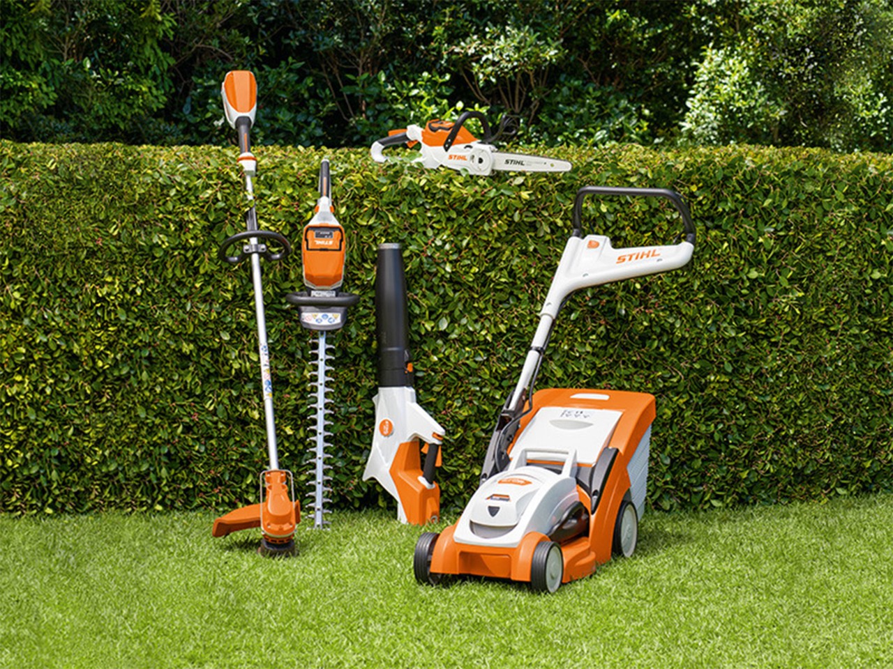 Geräte vor der Hecke stehend mit Rasenmäher, Heckenschere, Kettensäge, Freischneider und Sauglbläser