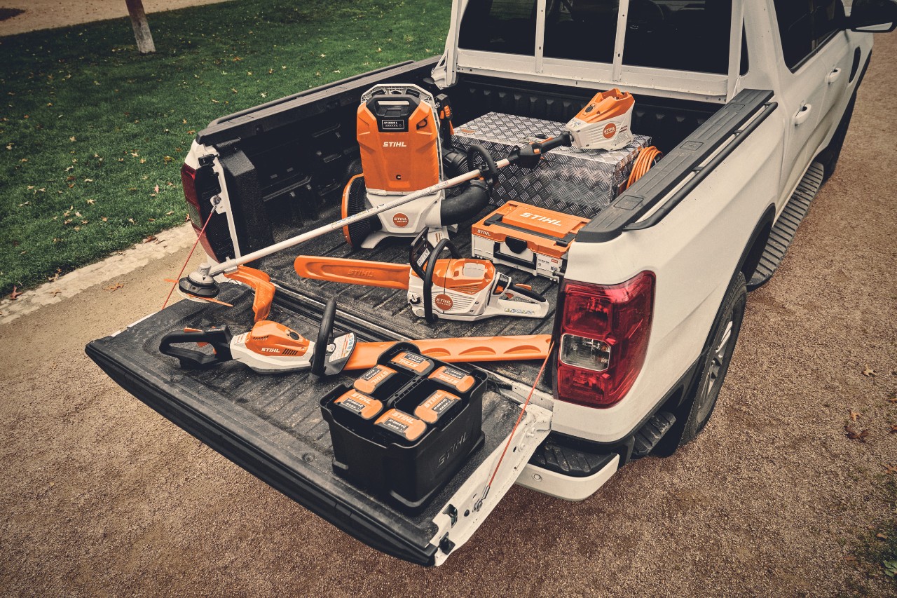 Ein Garten- und Landschaftsbauer Team steht vor einem Pritschenwagen auf dem STIHL Profi-Akku-Geräten liegen.