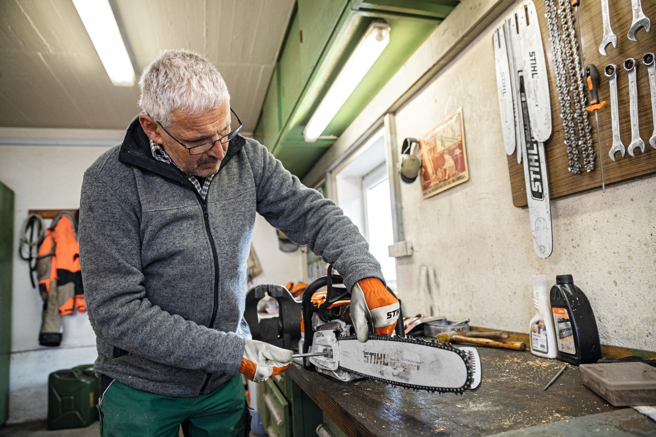 Ein Mann in einer Werkstatt schraubt an einer Motorsäge mit der Führungsschiene STIHL Rollomatic E 