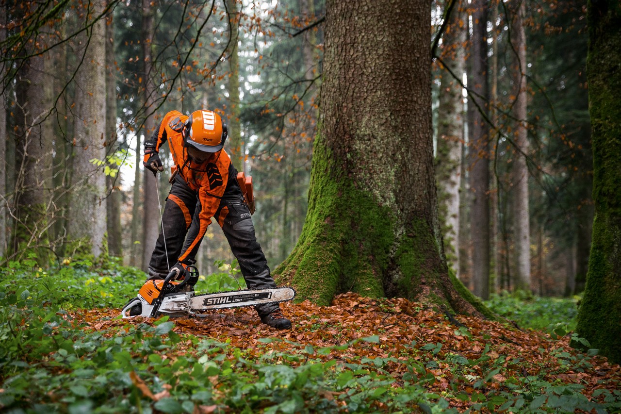Mann in Schutzkleidung startet STIHL Benzin-Kettensäge MS 500i im Laubwald auf dem Boden