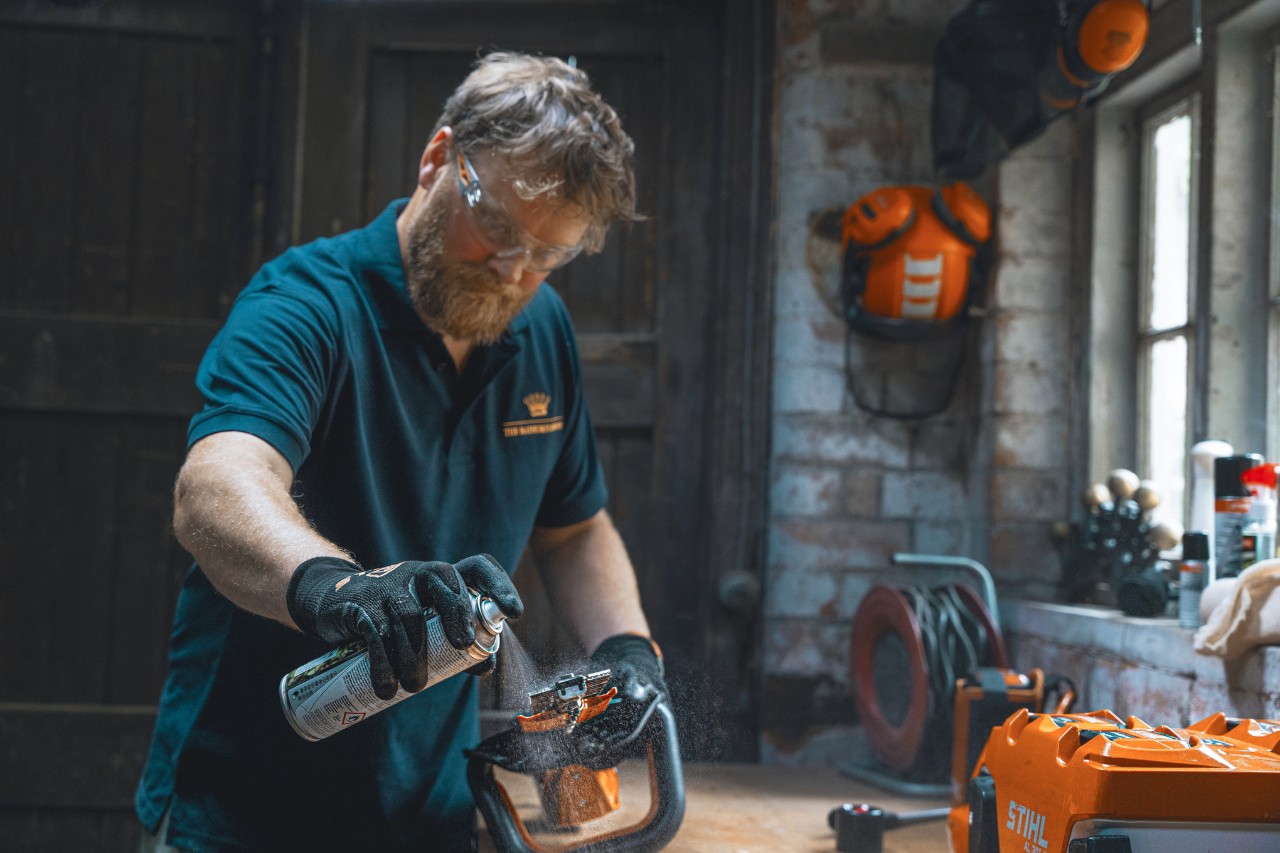 Ein Mann in einer Werkstatt sprüht eine Heckenschere mit STIHL Superclean ein