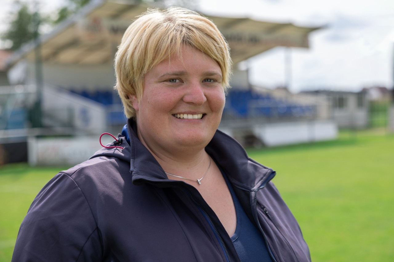 Greenkeeperin Lesly Huber steht auf dem Sportplatz SC Sand und lächelt in die Kamera