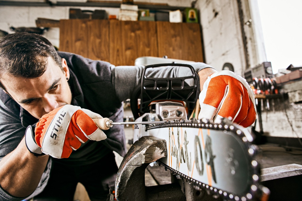 Mann mit STIHL Handschuhen feilt die Kette einer STIHL Benzin-Kettensäge 261 C-M mit einer Rundfeile