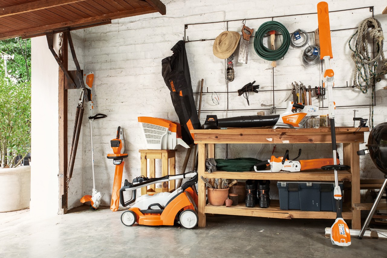 STIHL Akku-Motorsense FSA 56 wird hängend gelagert, daneben Akku-Heckenschere HSA 56 und HLA 56 und Akku-Rasenmäher RMA 339