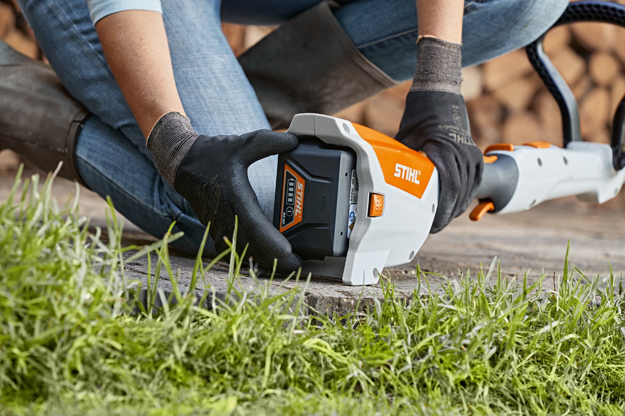 Person kniet auf dem Boden und entfernt einen Akku aus einer STIHL Akku-Motorsense FSA 57