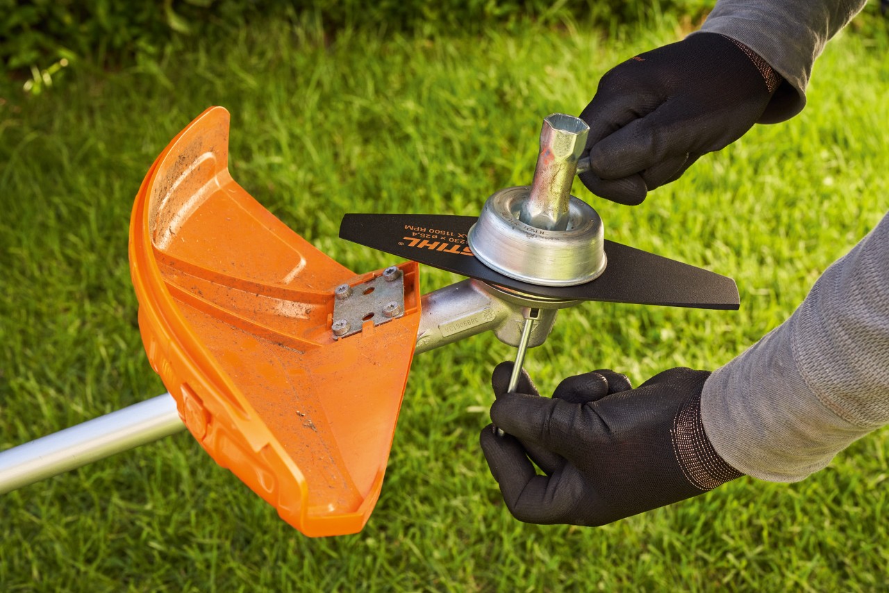 Person mit Schutzhandschuhen prüft Metallwerkzeug einer Motorsense