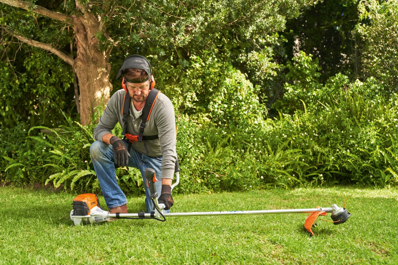 Mann legt die Benzin-Motorsense STIHL FS 91 auf den Boden, um sie zu starten