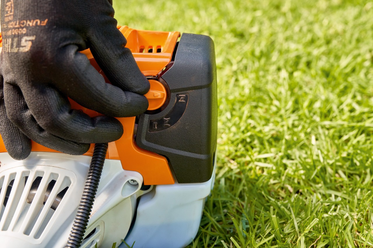 Mann stellt den Hebel der Kraftstoffpumpe der Benzin-Motorsense STIHL FS 91 ein, um sie zu starten