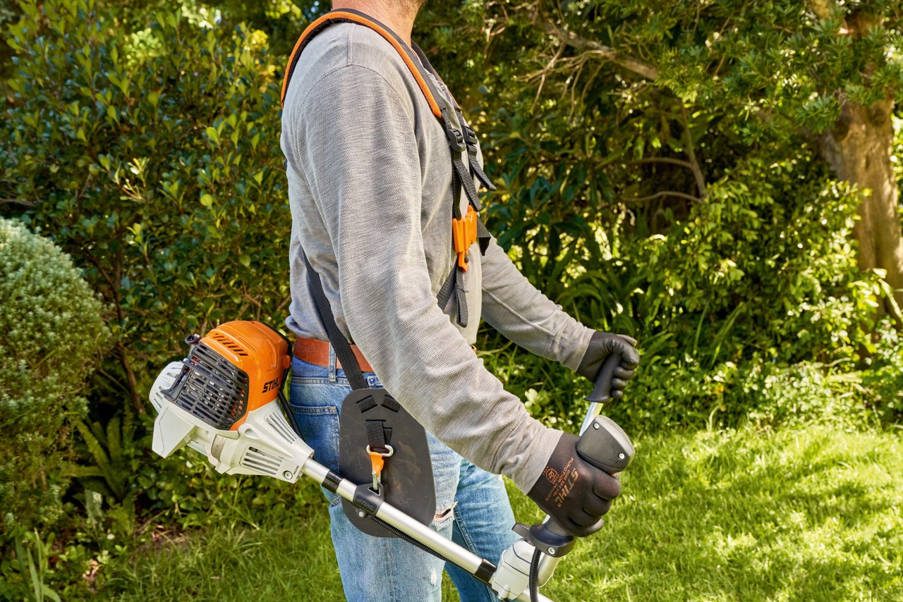 Mann hebt die Benzin-Motorsense STIHL FS 91 vom Boden auf, um mit dem Mähen zu starten 