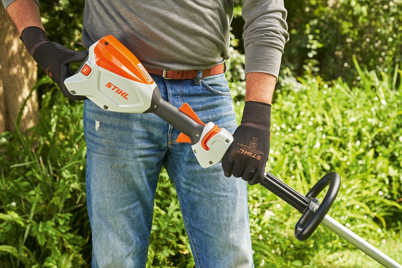 Mann mit Schutzhandschuhen überprüft den Akku der Akku-Motorsense STIHL FSA 60, um die Motorsense zu starten