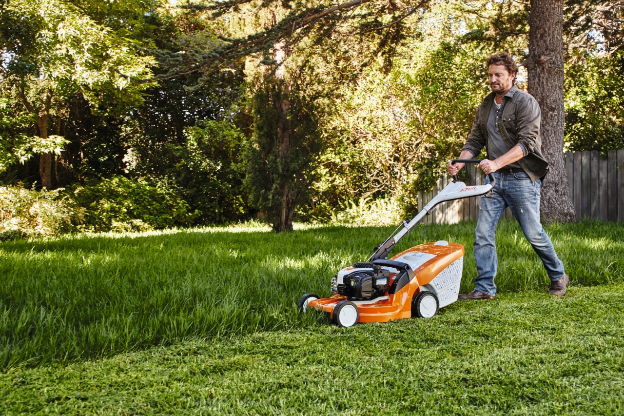 Ein Mann mäht in einem Garten den Rasen mit einem STIHL Rasenmäher 