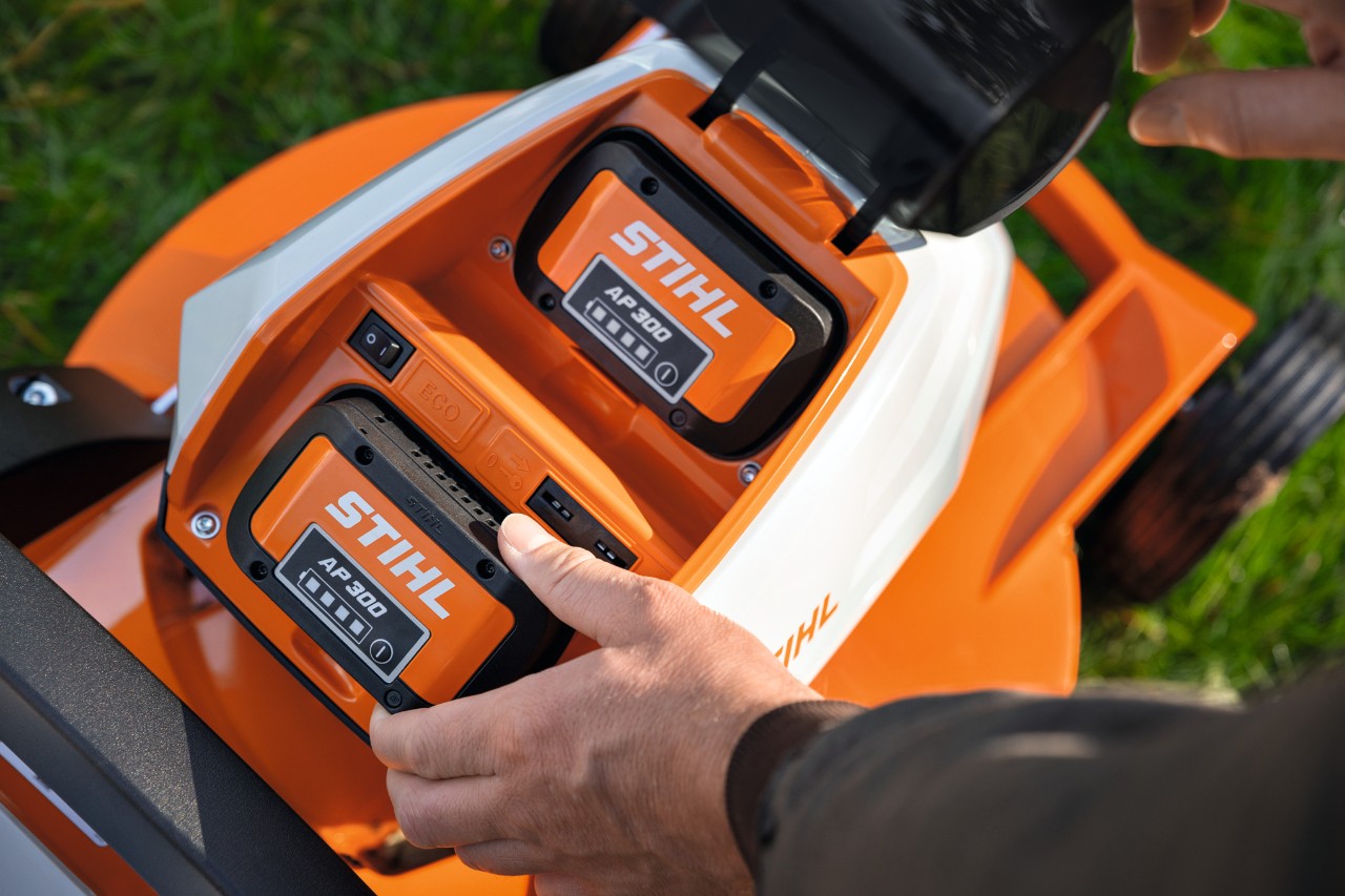 Eine Person legt den vollgeladenen Akku STIHL AP 300 in einen Rasenmäher ein