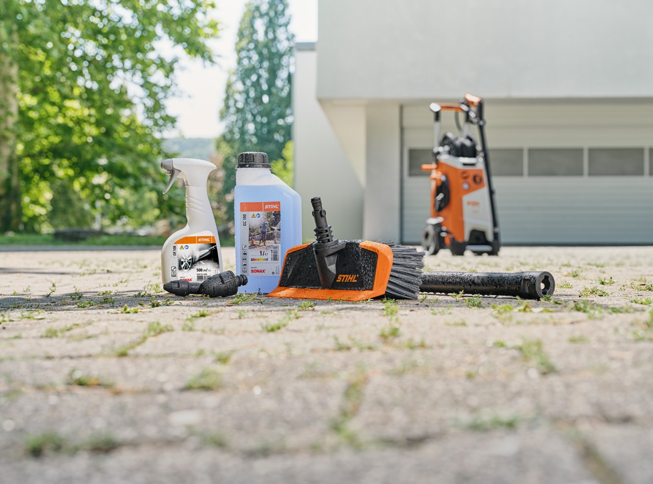 Reinigungsgeräte und Reinigungsmittel stehen am Boden vor einer Garageneinfahrt.