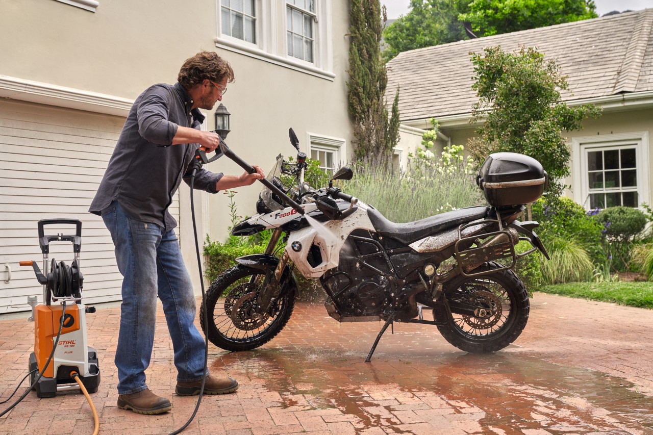 Mann in einer Garageneinfahrt reinigt Motorrad mit dem STIHL Hochdruckreiniger  