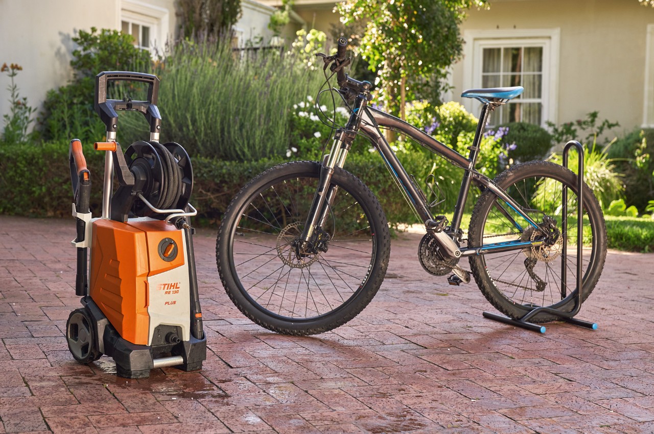 Ein Fahrrad steht nach dem Waschen vor einem Haus neben einem STIHL Hochdruckreiniger RE 130 plus 