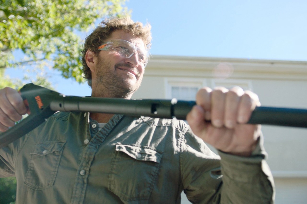 Mann mit Schutzbrille hält den Griff eines STIHL Hochdruckreinigers RE 130 plus vor einem weißen Haus