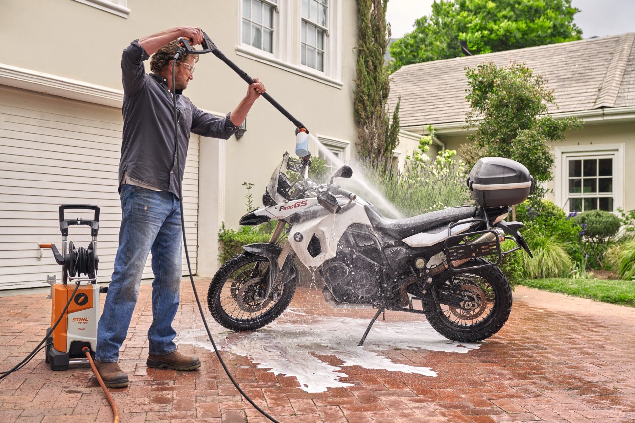 Mann sprüht Fahrzeugshampoo mit dem STIHL Hochdruckreiniger RE 130 plus, um Motorrad zu reinigen
