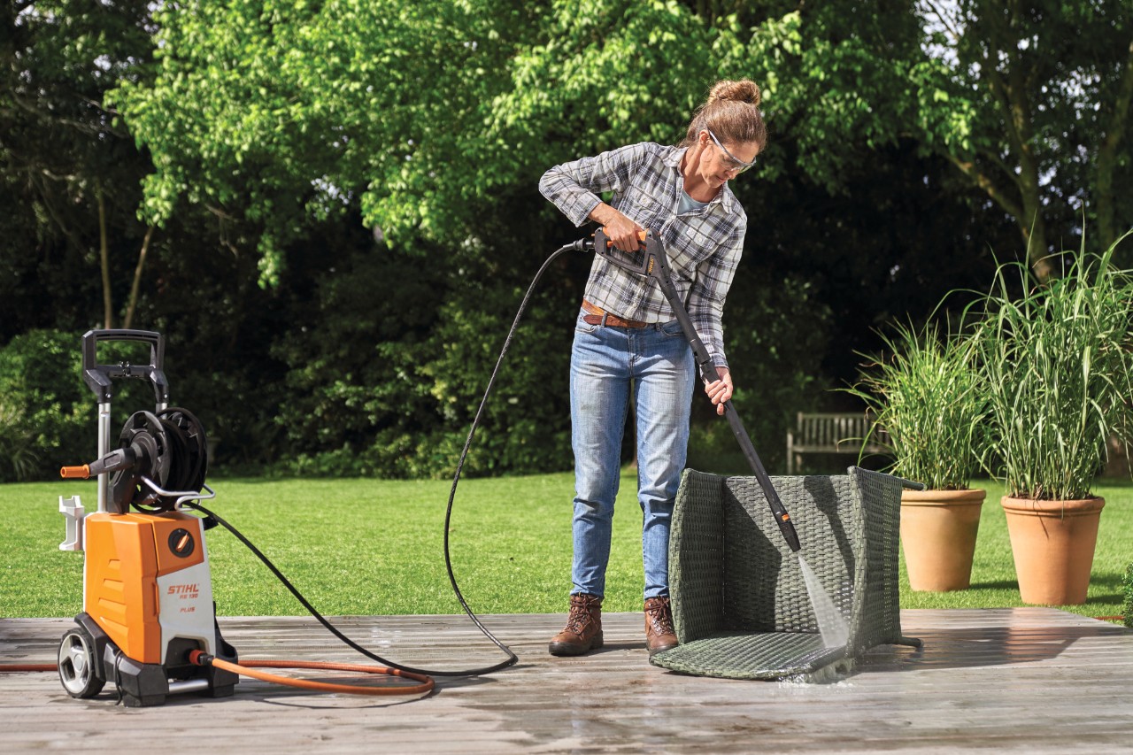 Frau reinigt Gartensessel aus Polyrattan auf der Terrasse mit STIHL Hochdruckreiniger RE 130 plus 