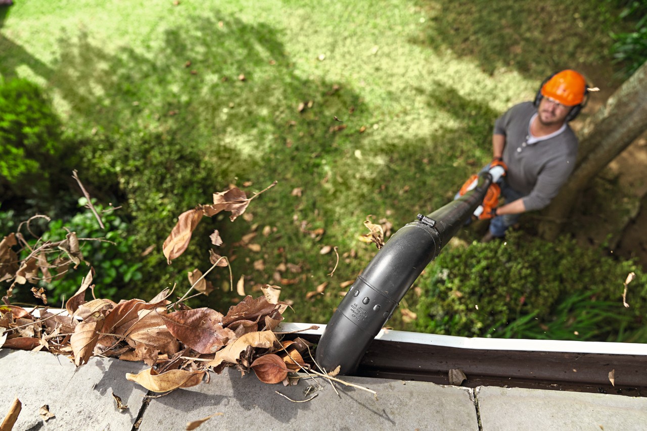 Mann reinigt Dachrinne mit STIHL Dachrinnenreinigungsset