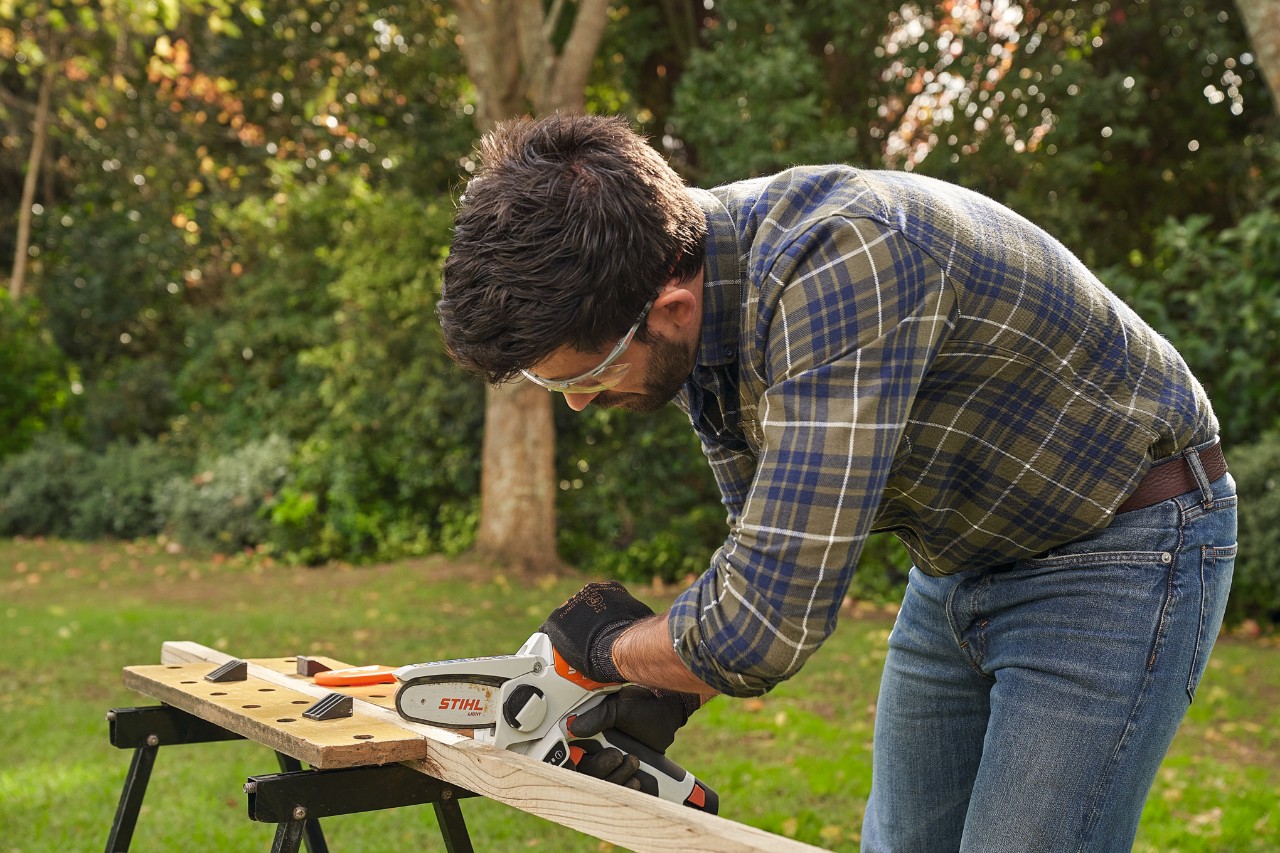 Ein Mann mit STIHL Schutzbrille und Schutzhandschuhen schneidet mit dem STIHL Akku-Gehölzschneider GTA 26 eine Holzlatte zu