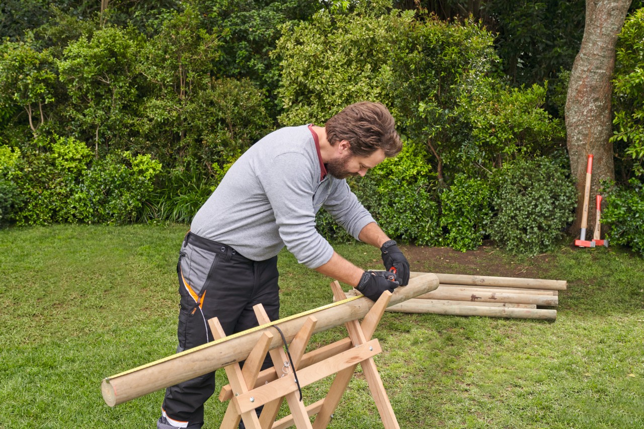 Ein Mann misst Äste auf einem Holzbock aus und kennzeichnet die Längen
