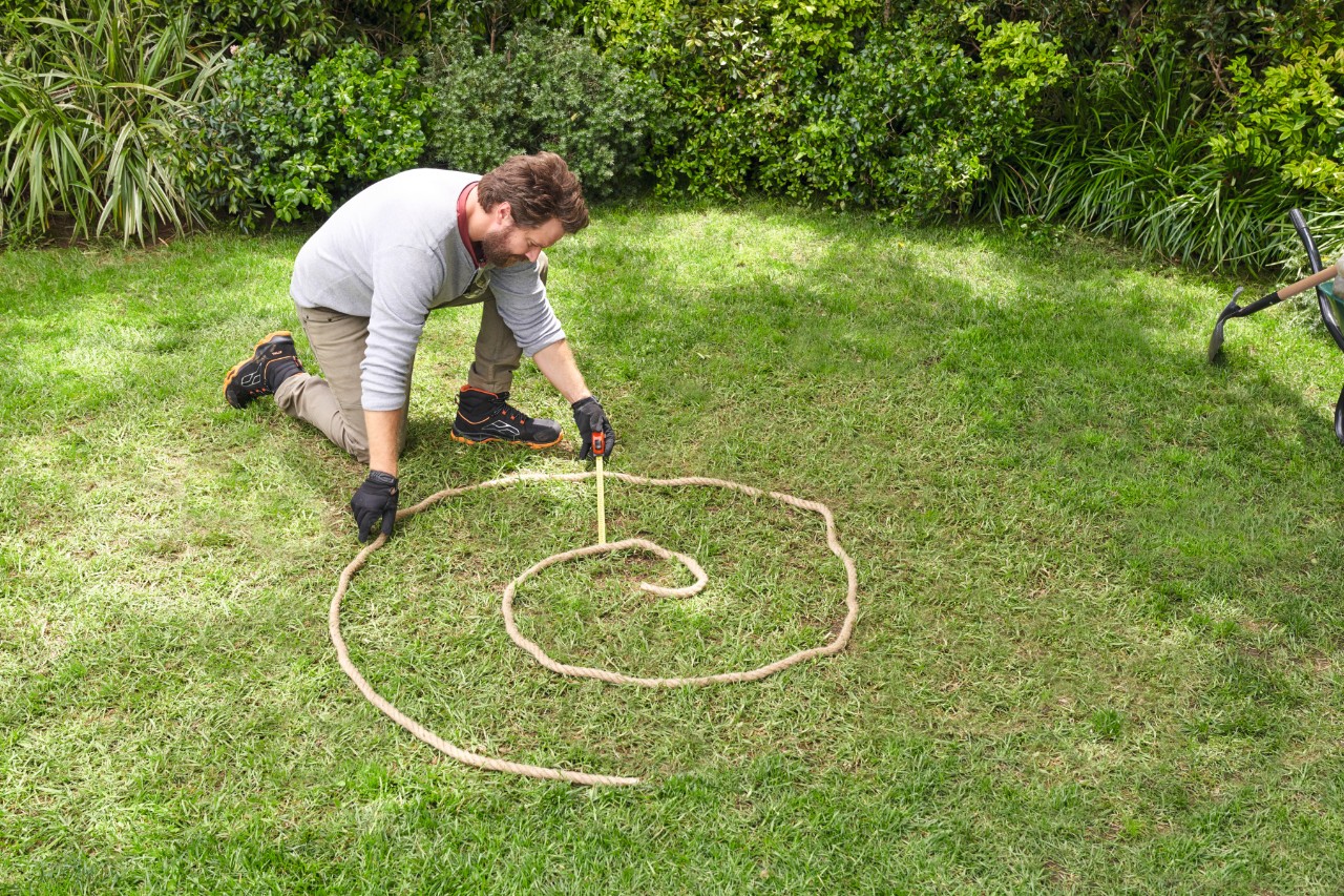 Ein Mann auf einer Rasenfläche markiert den geplanten Verlauf der Kräuterspirale mit einem Seil