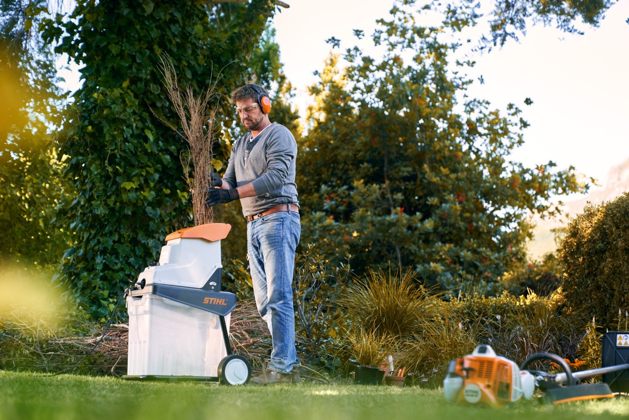 Mann mit Gehörschutz zerkleinert Äste vor dem Kompostieren mit einem STIHL Elektro-Häcksler GHE 140