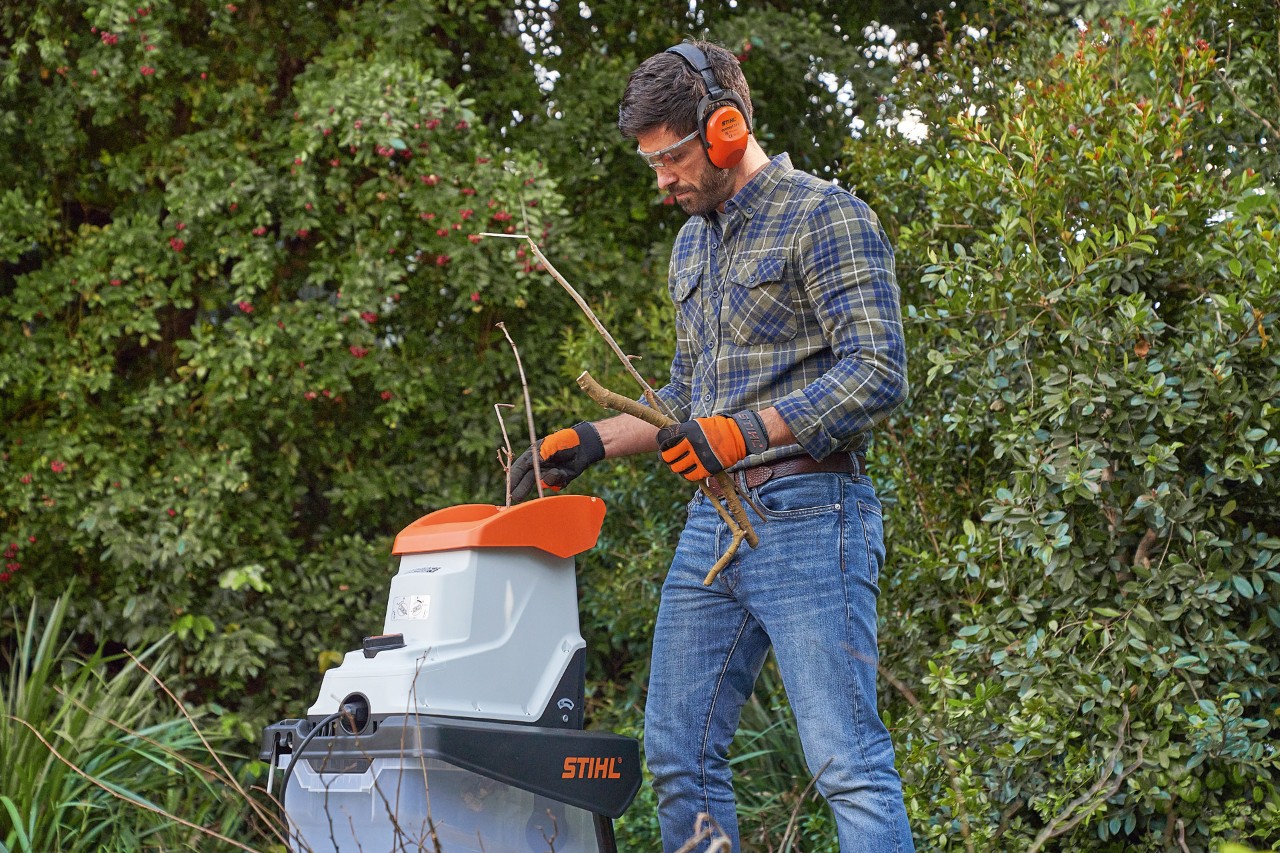 Ein Mann in Schutzausrüstung häckselt Zweige mit einem STIHL Gartenhäcksler  