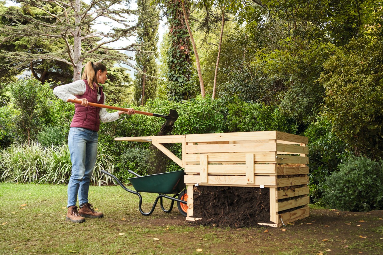 Eine Frau auf einem Gartengrundstück siebt Rohkompost neben einem selber gebauten Holzkomposter