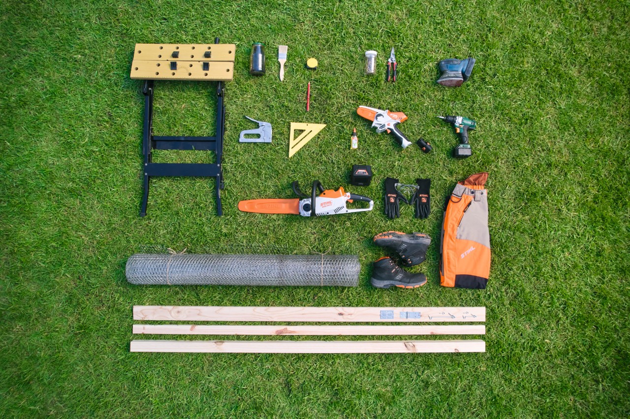 Vogelperspektive von nötigen Materialien und Werkzeugen, um einen Komposter selber zu bauen, nebeneinander angeordnet auf einer Wiese