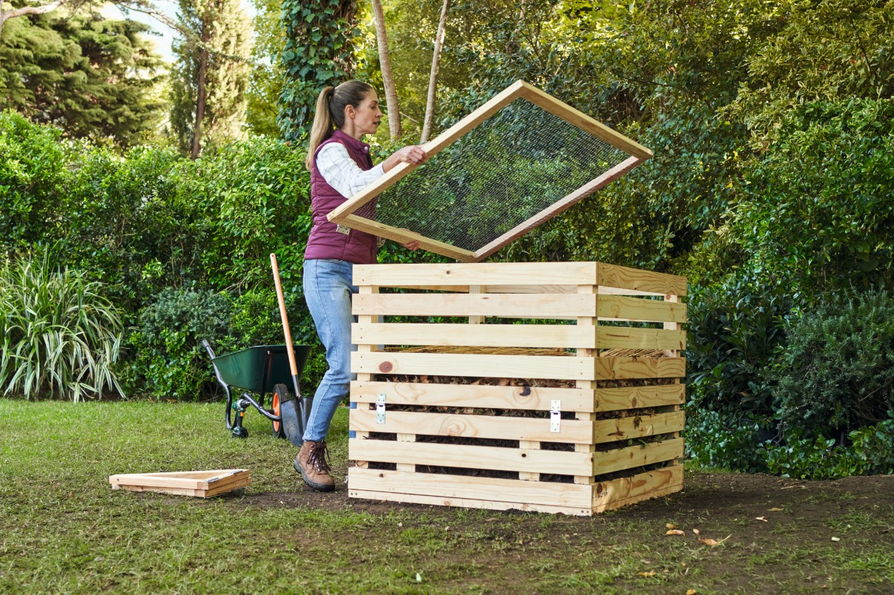 Eine Frau legt ein Durchwurfsieb auf einen selber gebauten Holzkomposter beim Kompost Anlegen