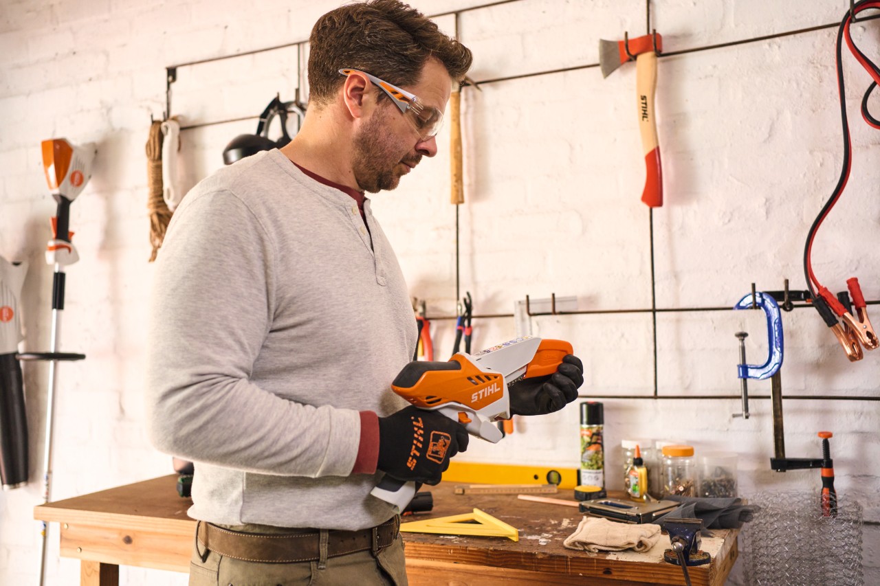 Ein Mann mit Schutzbrille nimmt die Schutzkappe des Akku-Gehölzschneiders STIHL GTA 26 ab