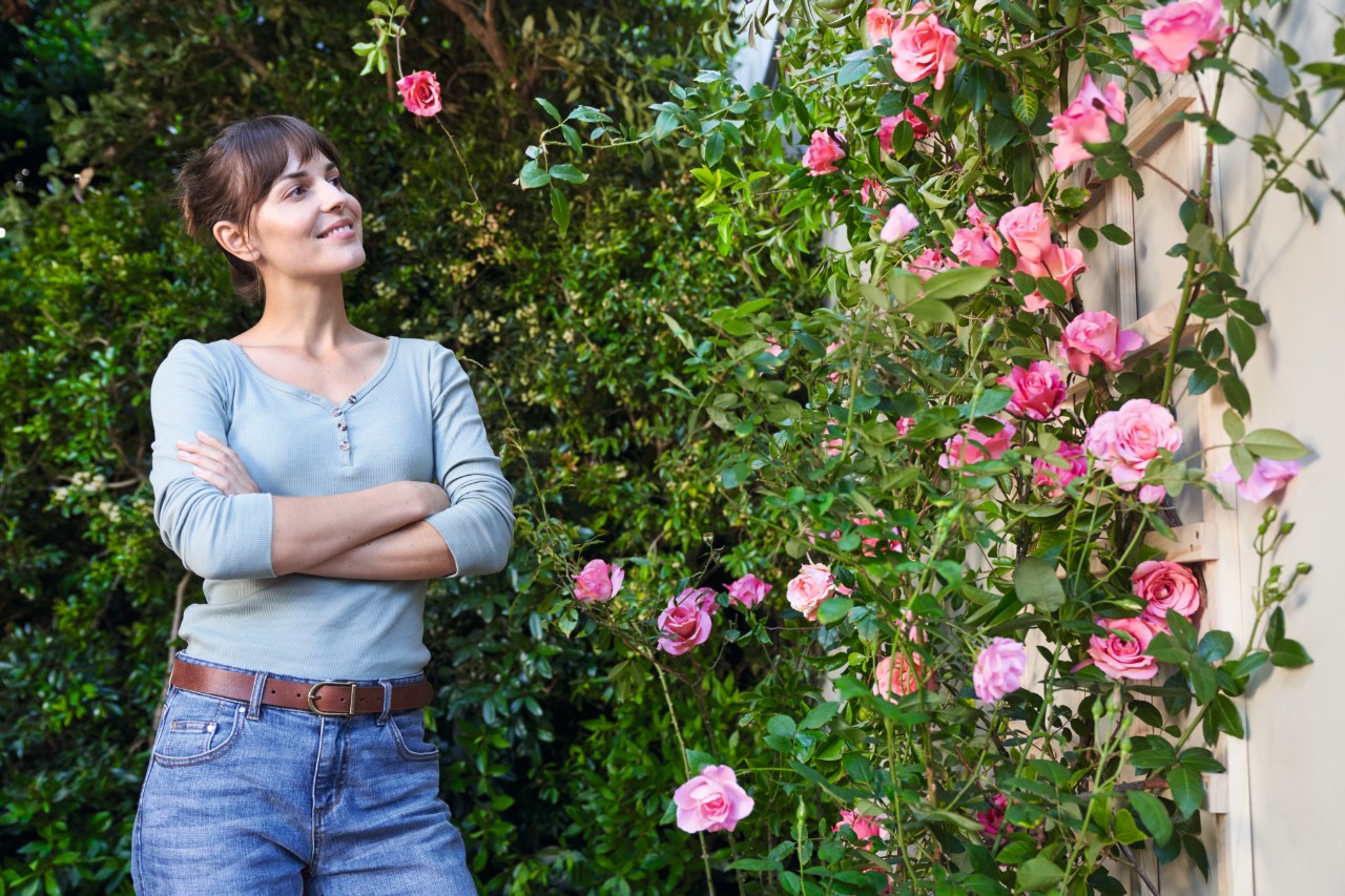 Frau steht vor einer mit Rosen blühenden Fassade