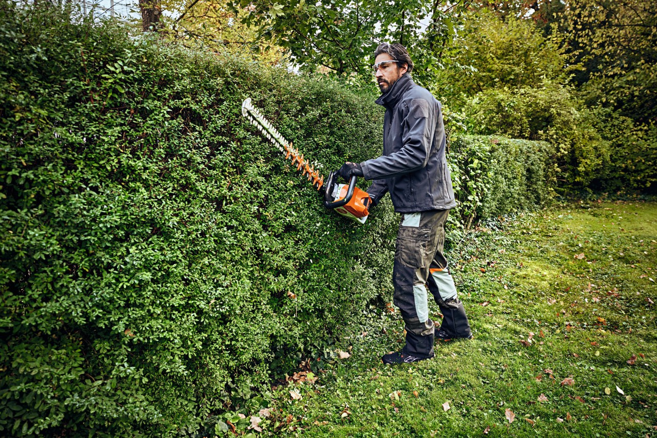 Ein Mann in Schutzausrüstung schneidet mit einem STIHL Heckenschneider eine Hecke 