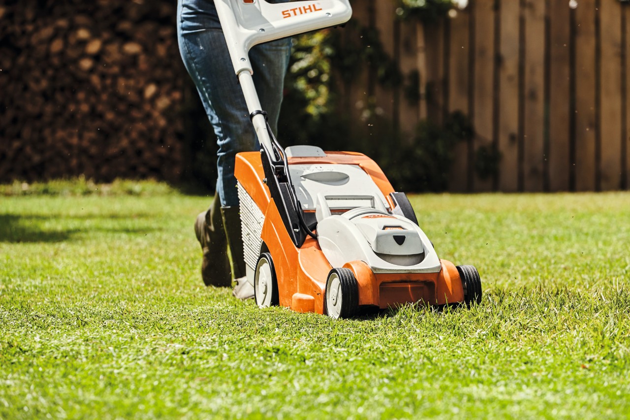 Nahaufnahme, wie jemand mit einem STIHL Rasenmäher eine Rasenfläche mäht 