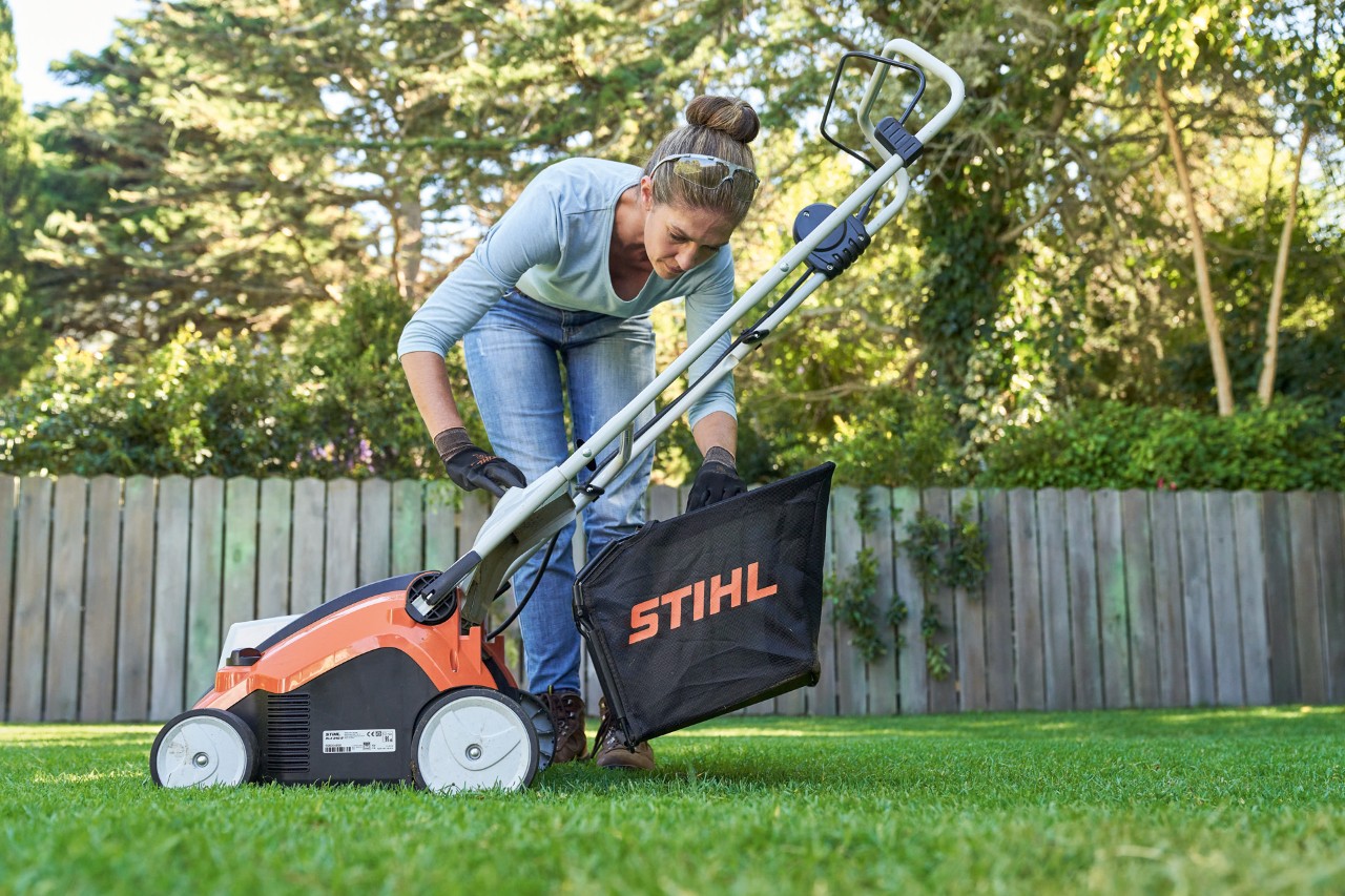 Frau hängt Fangkorb des STIHL Akku-Rasenlüfters RLA 240 Rasenlüfters hinten am Gerät ein.
