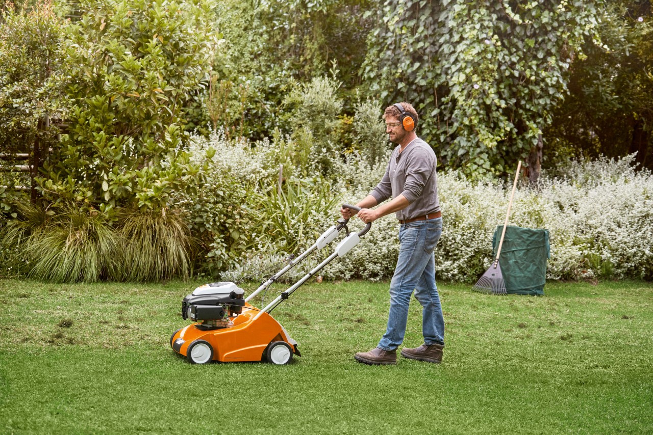 Mann vertikutiert grünen Rasen mit einem STIHL Benzin-Rasenlüfter RL 540