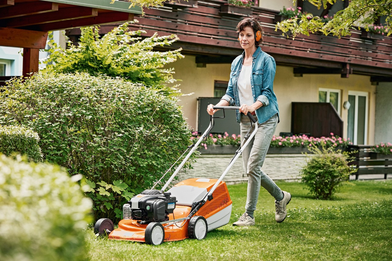 Frau betreibt Rasenpflege im Frühjahr mit einem STIHL Benzin-Rasenmäher RM 243 T im Garten vor einem Haus