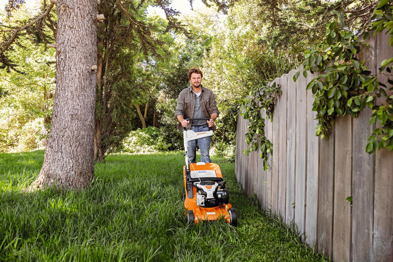 Mann betreibt mit STIHL Akku-Rasenmäher RMA 448 P-C auf einem bewachsenen Grundstück Rasenpflege im Sommer