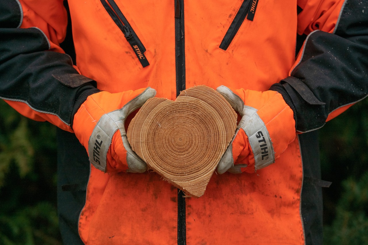 Person in STIHL Schutzkleidung hält ein Herz aus Holz 