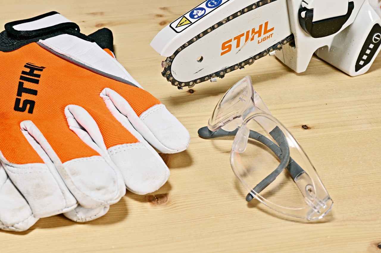 Schutzbrille, Handschuhe und STIHL Akku-Gehölzschneider GTA 26 auf Holzplatte