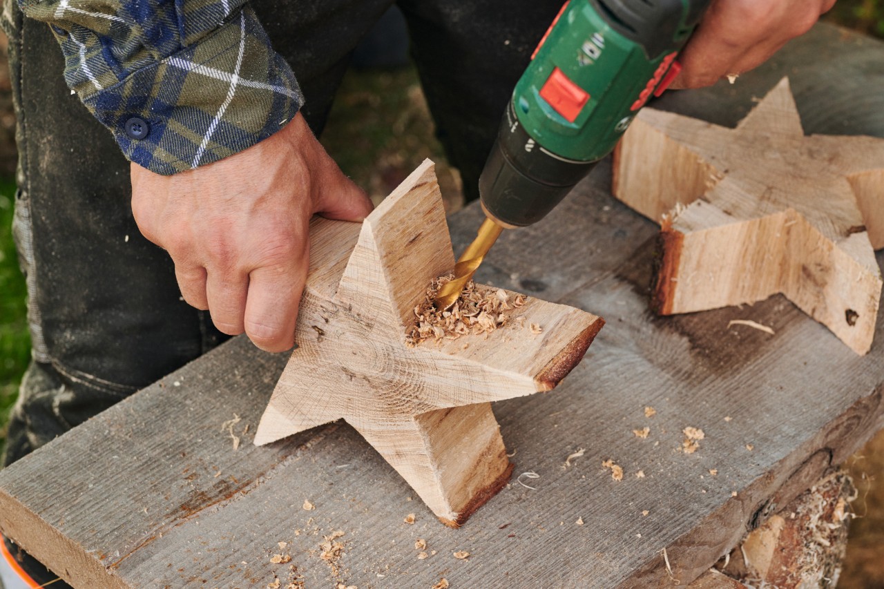 Mit Holzbohrer wird im Stern aus Holz im unteren Teil ein Loch gebohrt