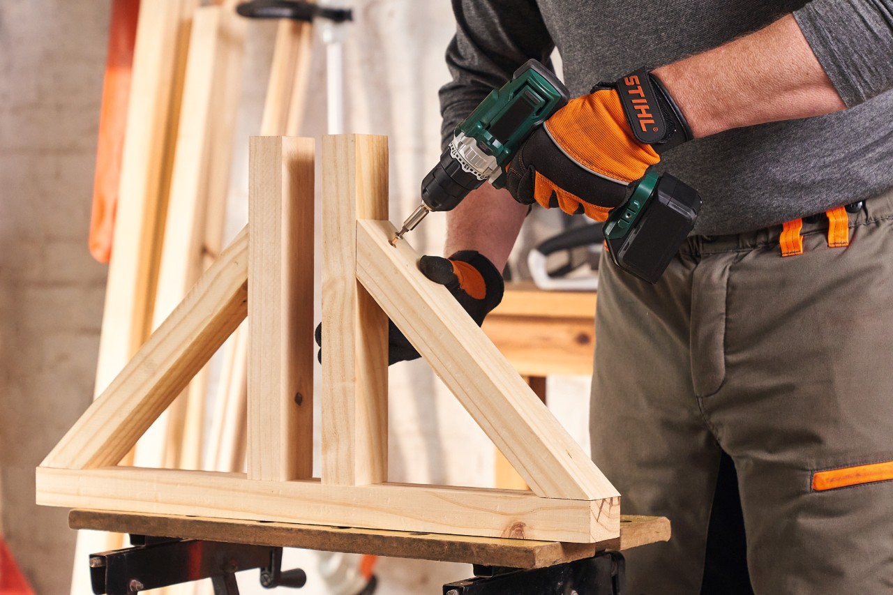 Person mit Schutzhandschuhen STIHL Function Protect schraubt die Füße für einen Sichtschutz aus Holz zusammen