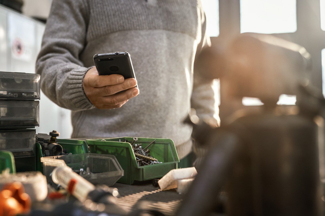 Person mit Smartphone in einer Werkstatt