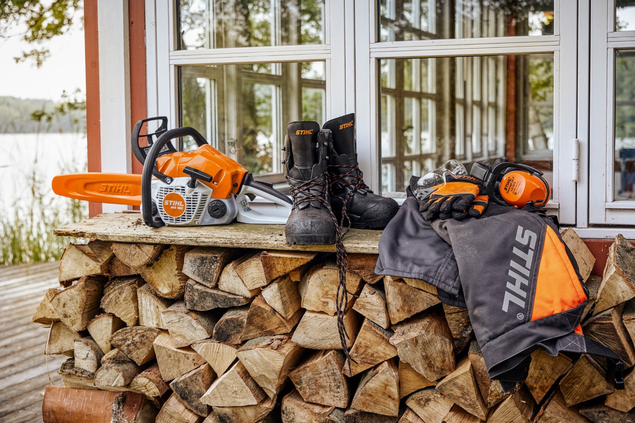 STIHL Schutzkleidung und die MS 162 liegen auf einem Regal über gestapeltem Brennholz