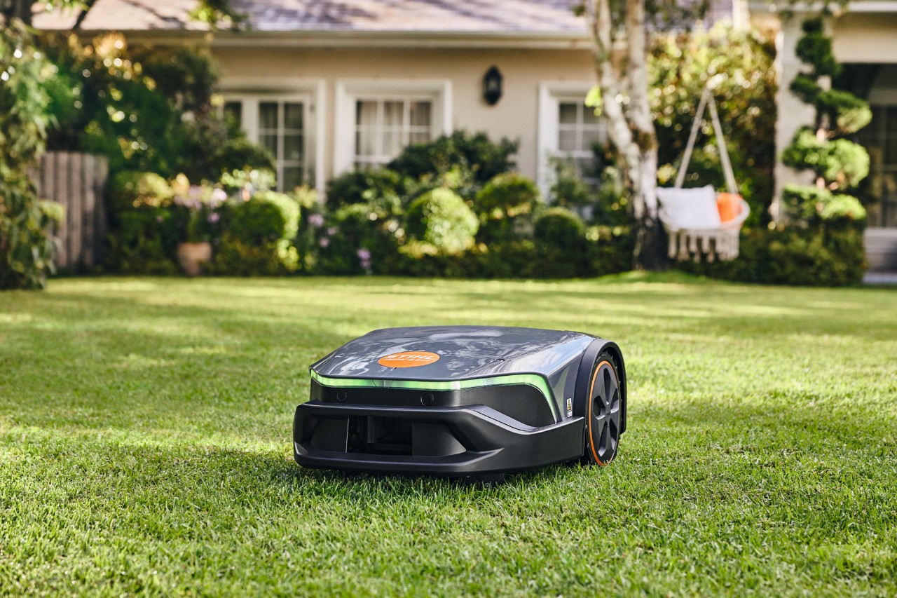 Ein iMOW® Evo mäht im Garten vor einem Haus und einer Hängematte den gut gepflegten Rasen.