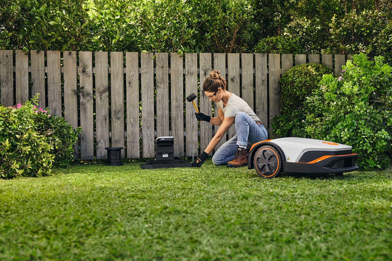 Eine Frau instaliert die Dockingstation für ihren STIHL iMOW® vor einem Zaun in ihrem Garten selbst.